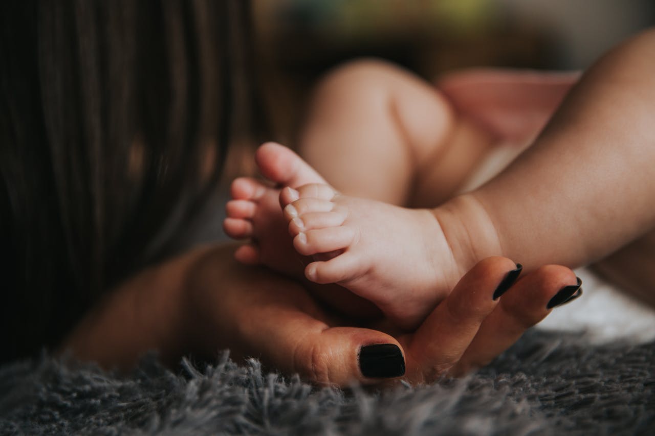 Person Holding Babys Feet in Selective Focus Photography